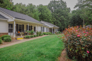 Two, one story apartment buildings with bushes and green grass.