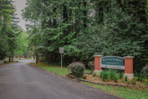 A wooded road with an entrance sign on the right side.