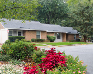 A one story brick apartment building with blooming bushes.