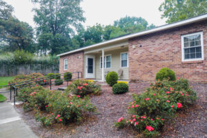 A one story brick building with blooming bushes