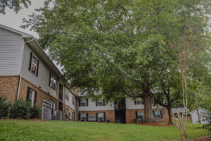 A two story apartment building with trees and a green lawn