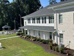 A two story white apartment building with bushes and grass