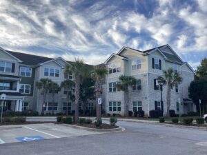 A three story apartment building with palm trees and a blue sky